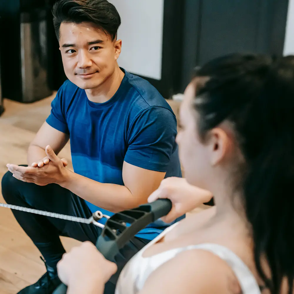 Fitness-valmentaja tukee asiakasta soutulaitteella: esimerkki henkilökohtaisesta otteesta, jonka verkkovalmennus mahdollistaa.